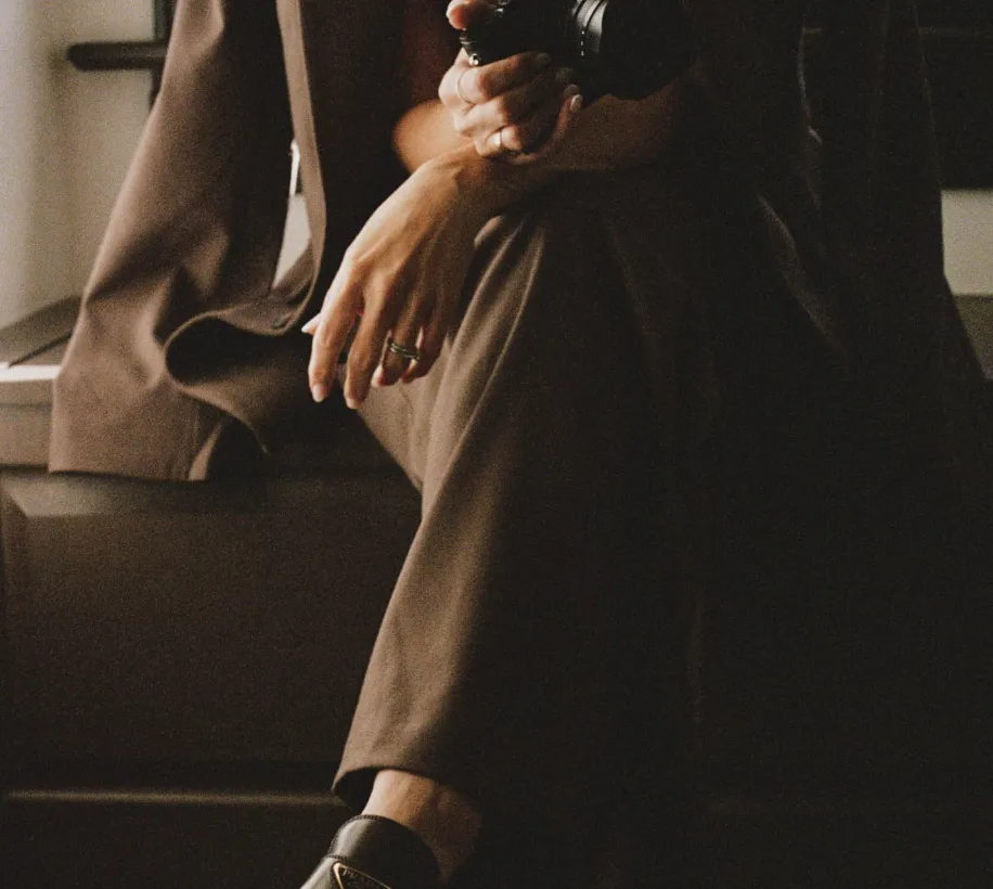 Cropped view of a person wearing a brown suit and black leather loafers while holding a camera